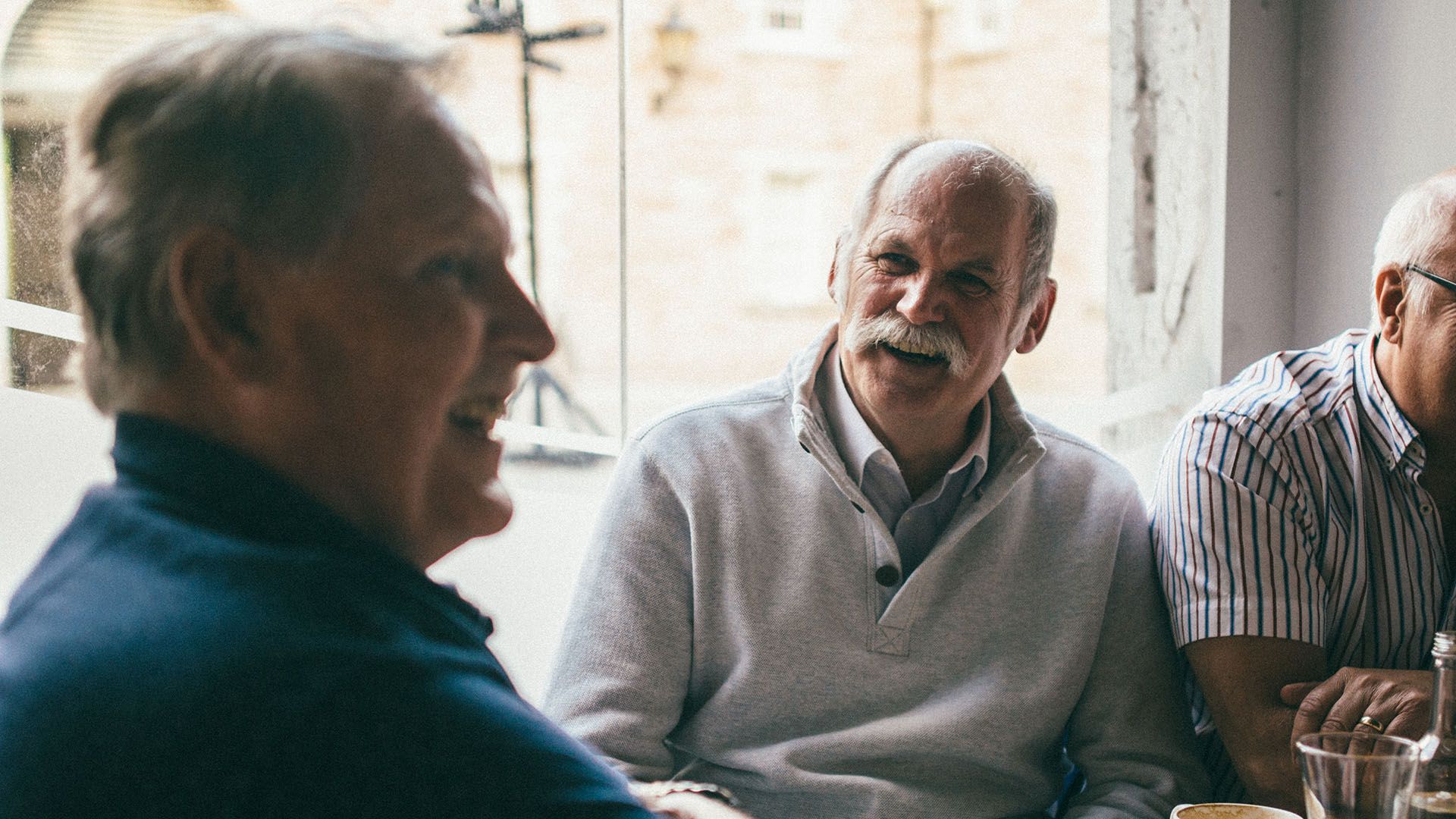 Photo of smiling grey-haired, senior men, sitting around a table.