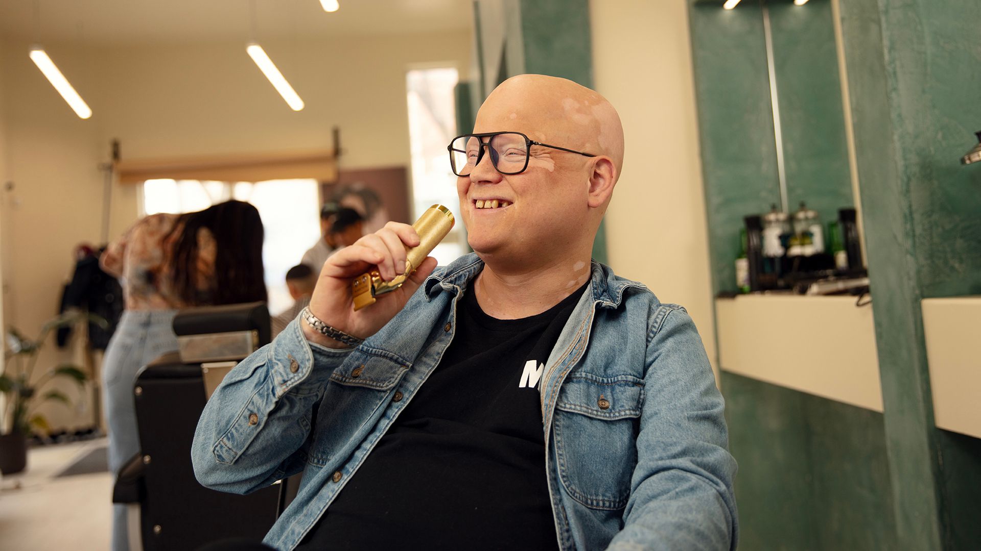 Comedian Simon Delisle poses in a barbershop chair, holding an electric shaver like it's his mic