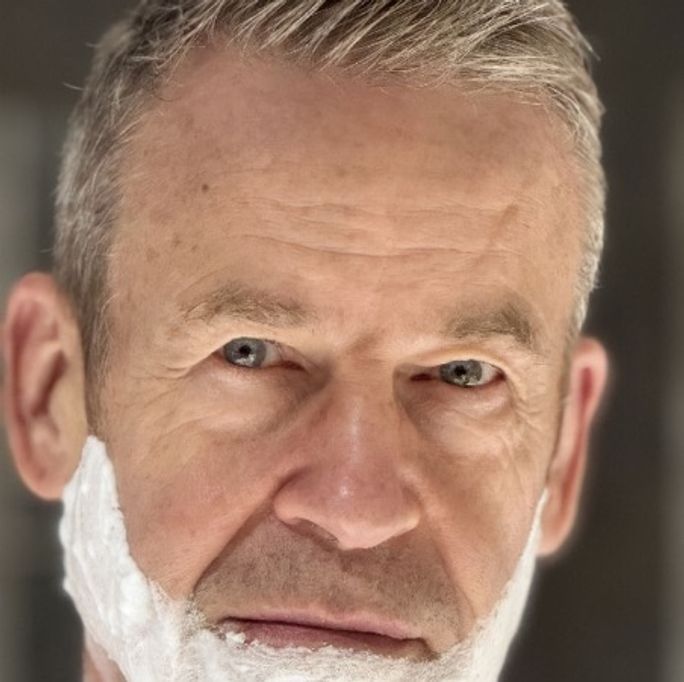 Portrait photo of a man, looking seriously to camera, his face lathered in shaving cream.