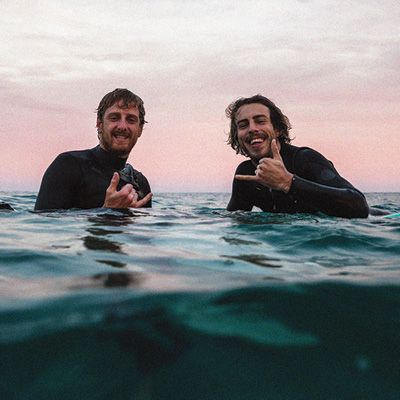 Two men in wetsuits, immersed chest-deep in water and looking to camera.