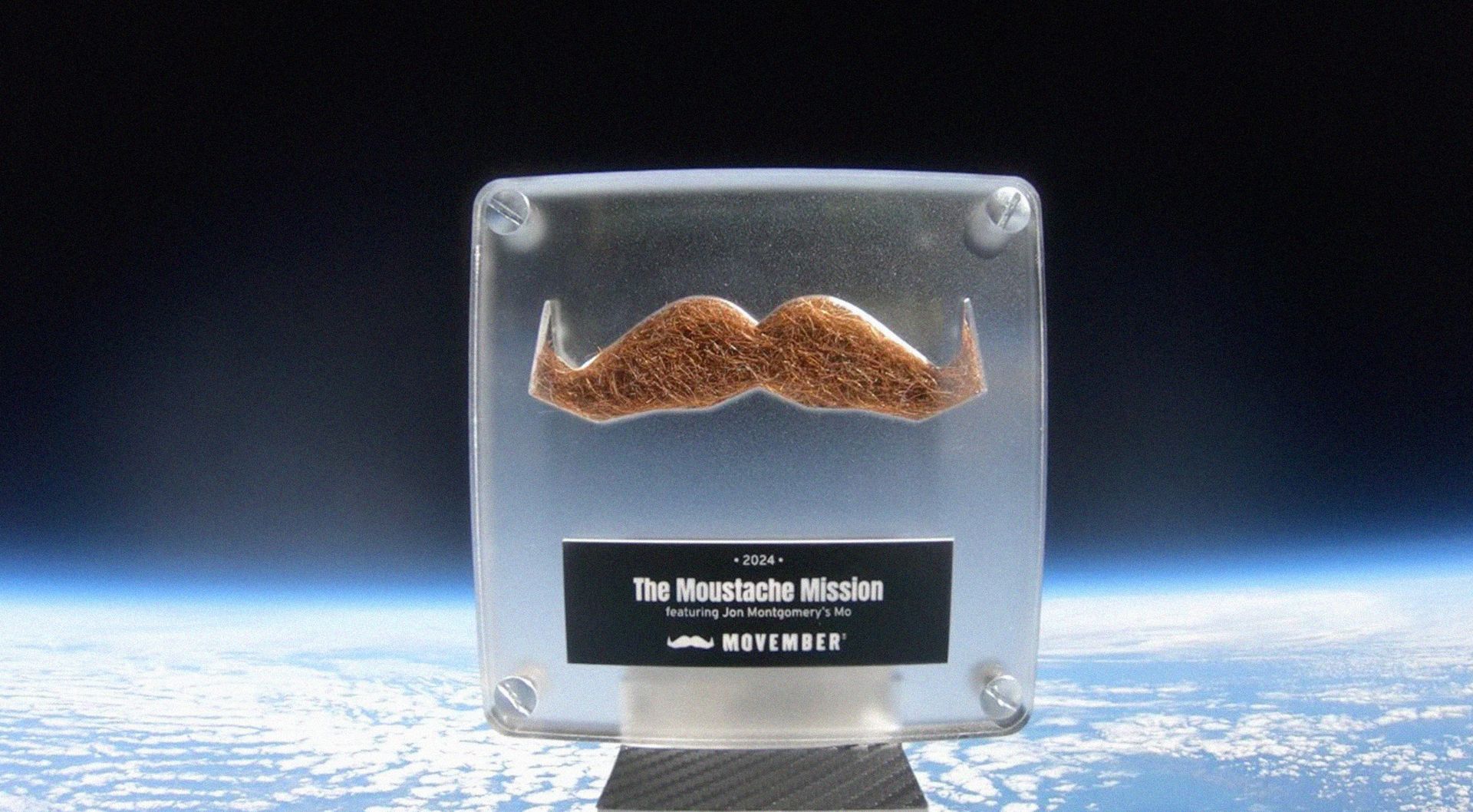 Photo of a shaved moustache encased in a transparent box, which has been sent to space. Behind is a view of the earth from space.