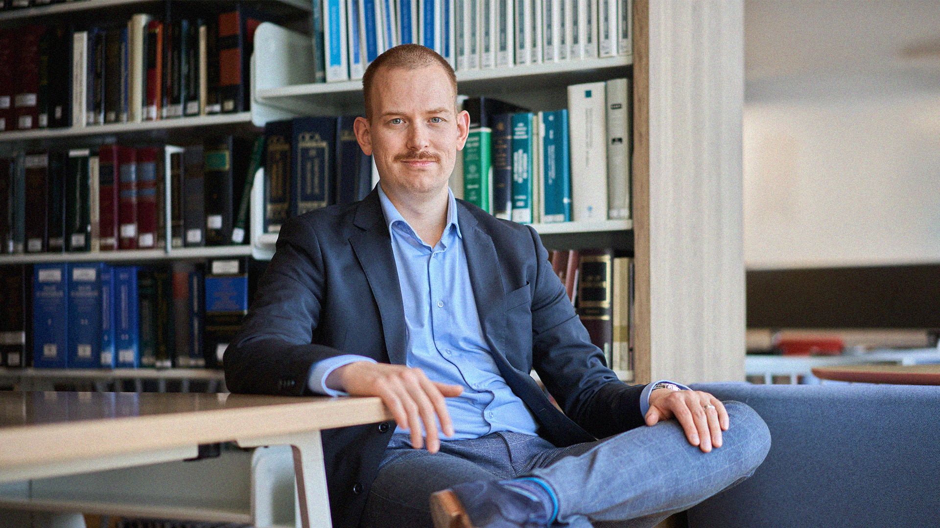 Man sitting in a chair in a law library soft smiling into the camera