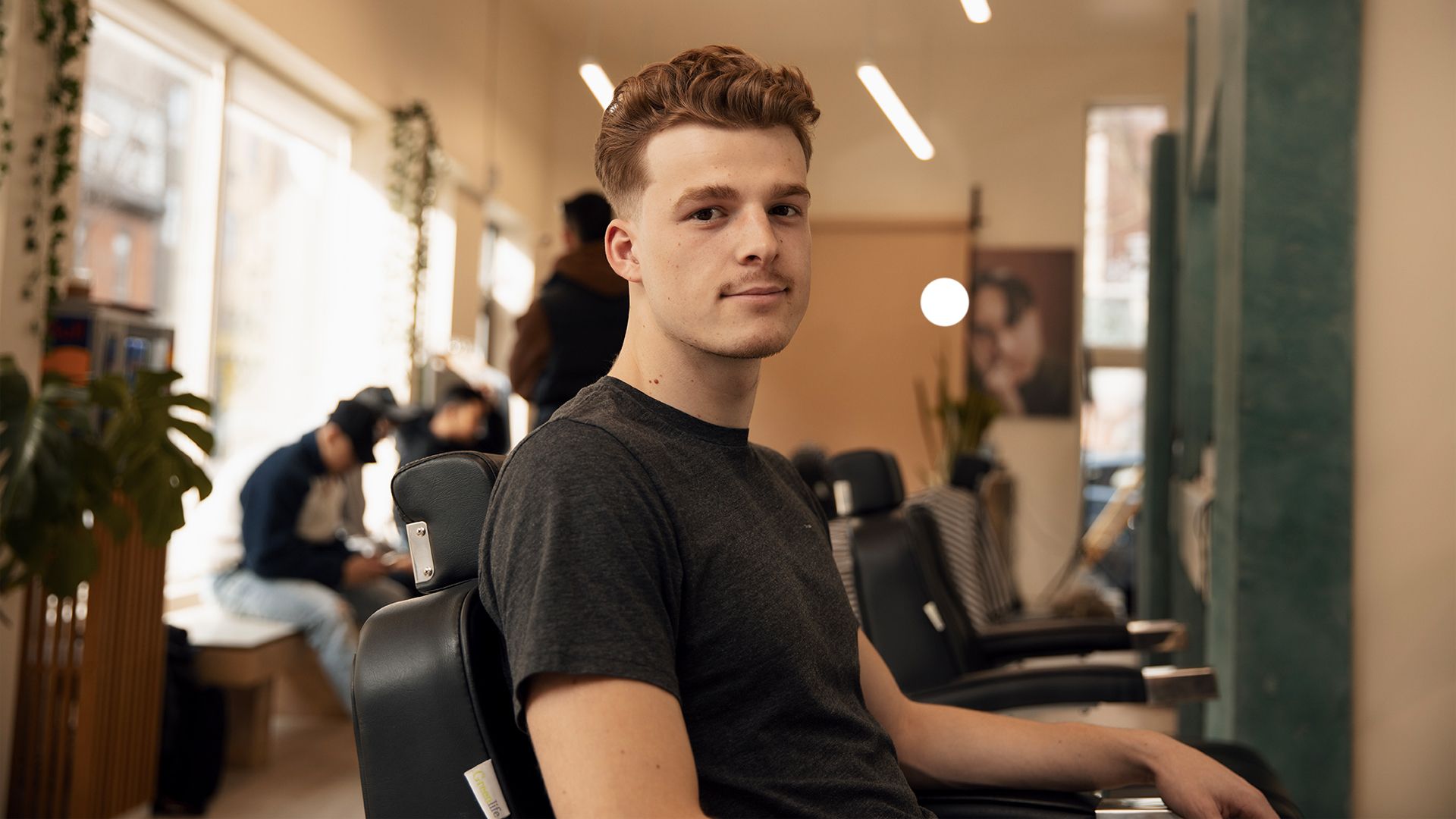 Young student smiles from the barber chair of a Montreal barbershop