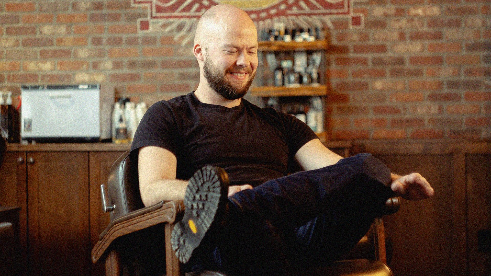 Photo of a man smiling and looking down while sitting in a barber chair 